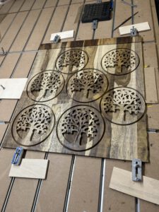 Mehrere runde Topfuntersetzer aus Holz mit filigranen CNC-gefrästen Baum- und Ornamentmotiven im Fertigungsprozess