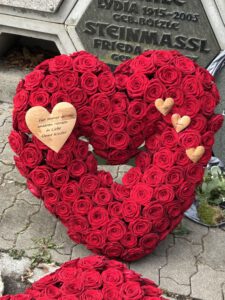 Herzförmige Trauergesteck aus roten Rosen mit mehreren kleinen gravierten Holzherzen.